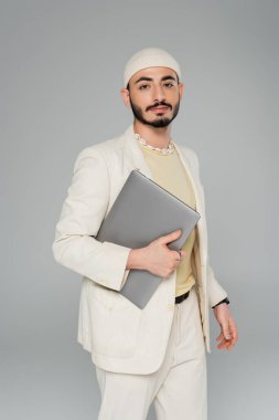 İyi giyimli, takım elbiseli homoseksüel bir adam elinde gri dizüstü bilgisayar tutuyor.  