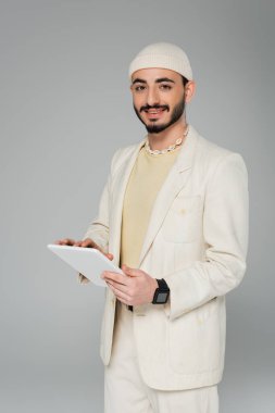 Gri üzerinde dijital tablet tutan pozitif ve şık bir gay.  