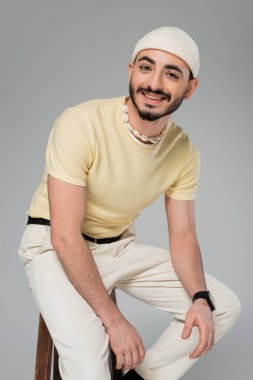Gri sandalyede oturan şapkalı neşeli gay adamın portresi.  