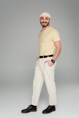 Gri arka planda poz veren şapkalı neşeli gay adam. 