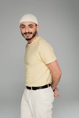 Gri renkli kameraya gülümseyen şapkalı ve deniz kabuğu kolyeli modaya uygun homoseksüel adam portresi.  