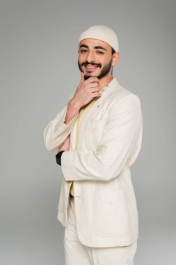 Şapkalı ve takım elbiseli neşeli eşcinsel adam gri renkli kameraya bakıyor.  
