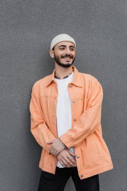 Moda ve pozitif gay şapkalı ve ceketli adam şehir sokağında duvarın yanında duruyor. 
