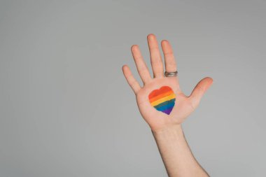 Cropped view of gay man with lgbt flag in heart shape on hand isolated on grey, International day against homophobia clipart