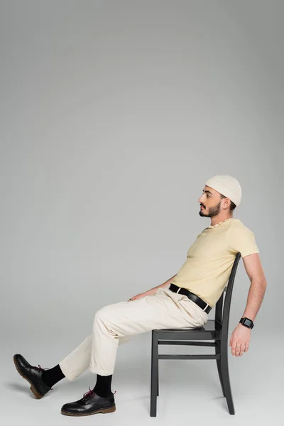 头戴米黄色帽子 留着胡子的基佬坐在灰色背景椅子上的侧视图 — 图库照片