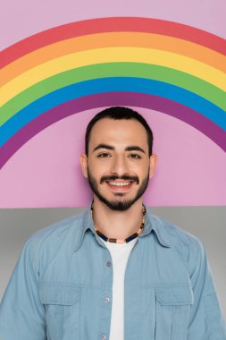 Gri üzerinde lgbt bayrağı olan ve plaketin yakınındaki kameraya bakan gülümseyen gay adamın portresi.  