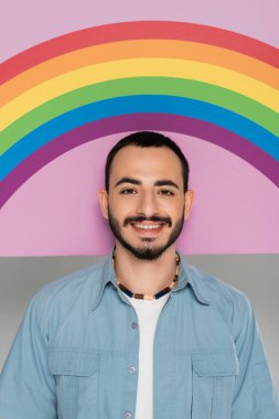 Portrait of smiling gay man looking at camera near placard with lgbt flag isolated on grey   clipart