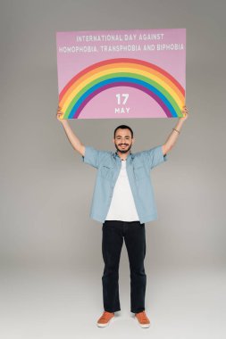 Homofobiye karşı uluslararası gün, transfobi ve gri yazılar üzerinde Bifobi yazan bir pankart tutan kaygısız eşcinsel adam. 