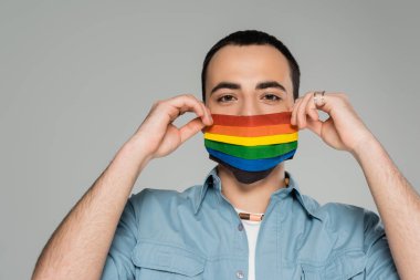 Igbt bayraklı sağlık maskeli genç homoseksüel adam gri renkte izole edilmiş.  
