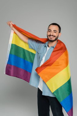 Igbt bayrağını tutan kaygısız gay adam ve gri kameraya bakıyor.  