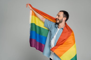 Sakallı ve neşeli eşcinsel adam elinde Igbt bayrağı ve gri, Uluslararası Homofobiye Karşı Günü 'nde izole bir şekilde bakıyor.