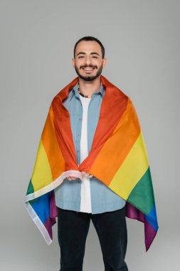 Neşeli gay adam kameraya bakıyor ve elinde lgbt bayrağı tutuyor. Gri, Uluslararası Homofobiye Karşı Gün
