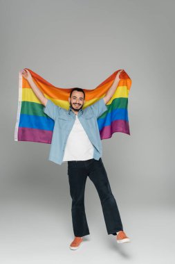 Gri arka planda lgbt bayrağı tutan tam boy homoseksüel adam. 
