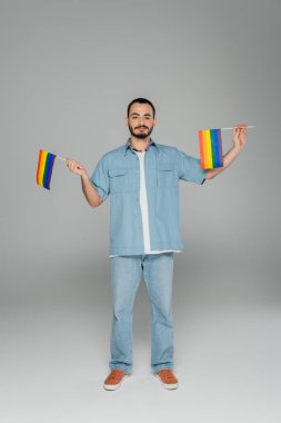 Gri arka planda dururken elinde lgbt bayrakları tutan genç eşcinsel adam Uluslararası Homofobiye Karşı Gün 