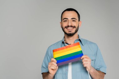 Gri üzerinde Igbt bayrağı taşıyan tişörtlü neşeli gay adamın portresi  