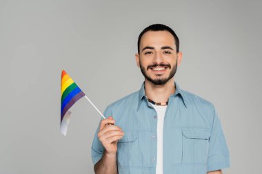 Gri, Uluslararası Homofobiğe Karşı Günü 'nde elinde lgbt bayrağı tutan gülümseyen ve sakallı eşcinsel adam portresi 