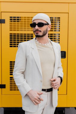 Şapkalı ve güneş gözlüklü modaya uygun homoseksüel adam şehir caddesinde duruyor. 