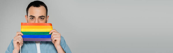 Брюнетка гомосексуальный мужчина покрывает лицо с lgbt флаг изолирован на сером, баннер 
