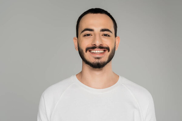Portrait of smiling gay man in white t-shirt looking at camera isolated on grey  