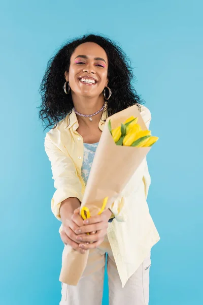 喜形于色的非洲裔美国女人 双手张开 手里拿着一束黄色郁金香 与蓝色隔离 — 图库照片