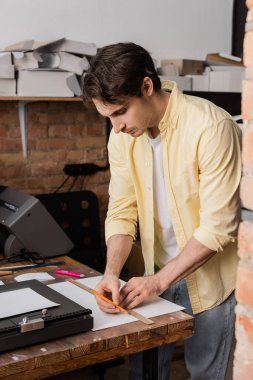 good looking printing operator holding ruler and pencil near paper in modern print center  clipart