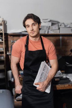 young typographer in apron holding newspapers with economic news   clipart