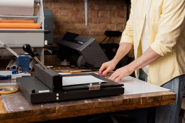 Baskı merkezinde kağıt budayıcı yanında bıçakla kağıt kesen tipografın kırpılmış görüntüsü 