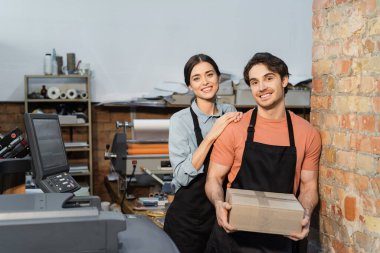 cheerful typographer leaning on happy colleague with carton box  clipart