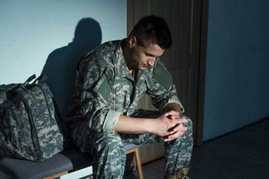 Evde koridorda otururken travma sonrası stres bozukluğu çeken üniformalı bir asker. 