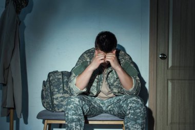 Depressed and lonely soldier in uniform sitting in hallway at home at night  clipart
