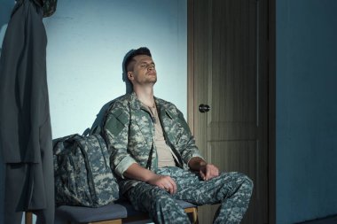 Military soldier with anxiety sitting in hallway on bench at night  clipart