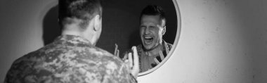 Black and white photo of stressed soldier with emotional distress screaming near mirror at home, banner  clipart