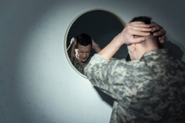 Stressed military veteran suffering from post traumatic stress disorder near mirror at home at night  clipart