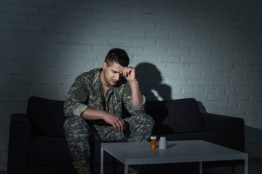 Frustrated military veteran with ptsd looking at pills on table at night time  clipart