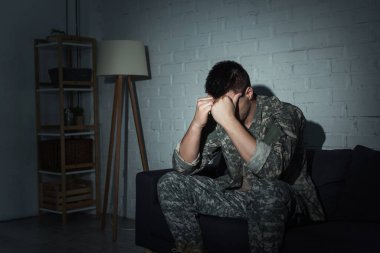 Military veteran in uniform suffering from emotional distress at home at night  clipart