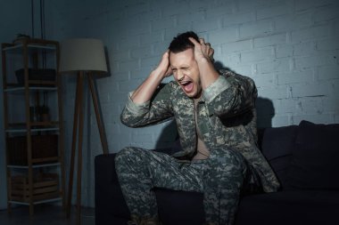 Irritated military veteran screaming while suffering from emotional distress at home at night  clipart