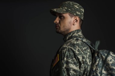 Kamuflaj üniformalı vatansever asker siyah bir sırt çantasıyla ayakta duruyor. 