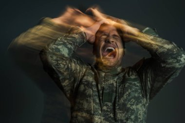 long exposure of soldier in uniform screaming while suffering from dissociation disorder isolated on dark grey  clipart