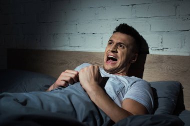 scared young man having nightmares and screaming at night  clipart