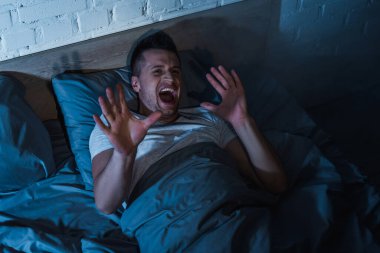 top view of scared young man with ptsd having nightmares and screaming at night  clipart