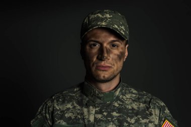 military man with dirt on face standing in uniform and cap isolated on grey  clipart