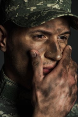 Yüzü kirlenmiş stresli asker yüzüne dokunuyor ve yüzünü çeviriyor. Travma sonrası stres bozukluğundan muzdarip. 