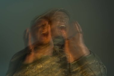 long exposure of soldier suffering from post traumatic stress disorder and screaming isolated on grey  clipart