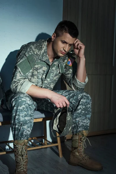 Frustrated American military veteran in uniform sitting in hallway at home at night