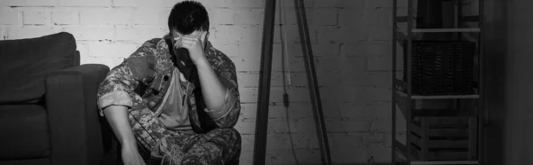 Black and white photo of military veteran suffering from emotional distress at home, banner