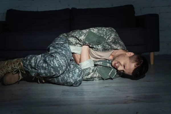 暗い部屋の床に横になっている間に心的外傷後ストレス障害に苦しむ軍の制服を着た不安サービスマン — ストック写真