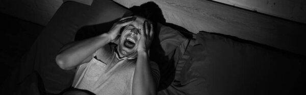 monochrome photo of young man screaming while having nightmares and panic attacks at night, banner 