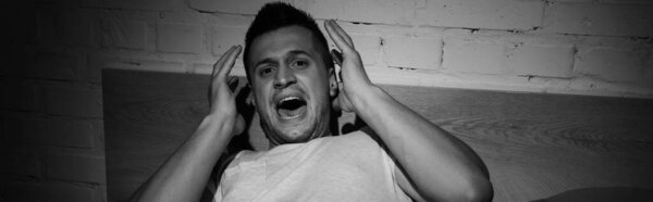 monochrome photo of stressed man with panic attacks screaming at night, banner 