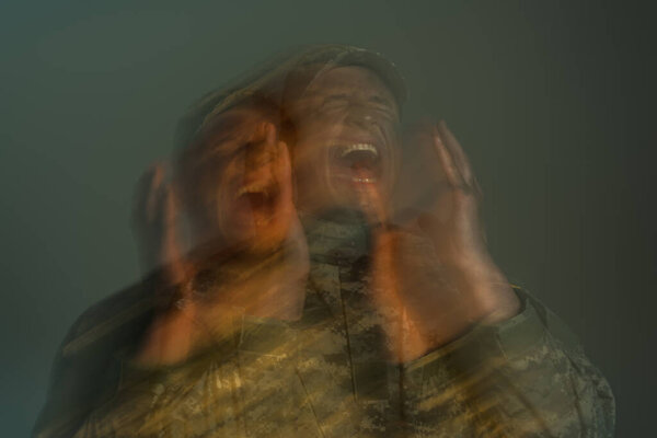 long exposure of soldier suffering from post traumatic stress disorder and screaming isolated on grey 