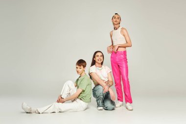 Bir grup neşeli genç lgbt topluluğu. Renkli giysiler içinde insanlar birlikte otururken gülümsüyor ve stüdyoda gri arka planda gurur gününü kutluyorlar. 
